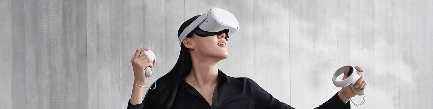 A woman wearing a virtual reality headset, holding two controllers, looking up to the top left.