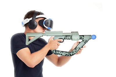 Man facing right wearing PSVR headset and black over the year headphones holding a rifle-like VR controller  